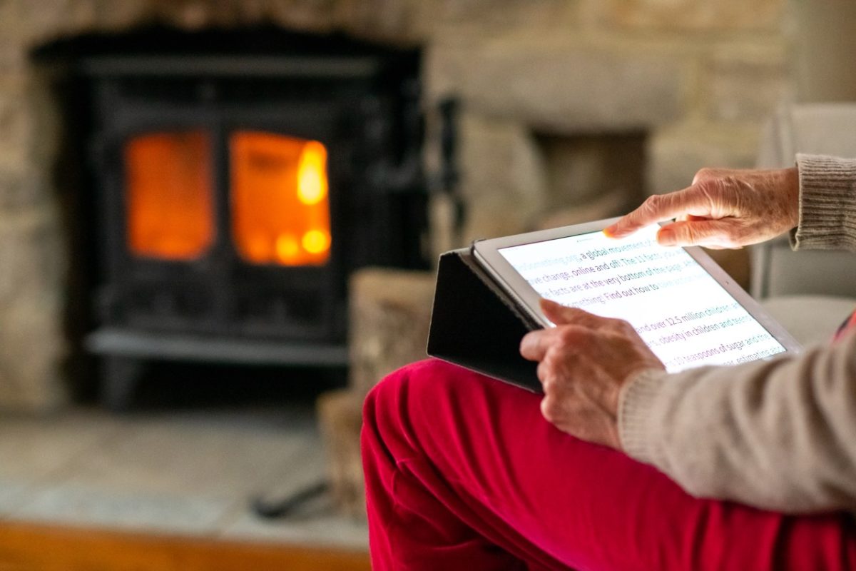 Eine Seniorin bedient auf ihrem Sofa einen Tablet-PC.