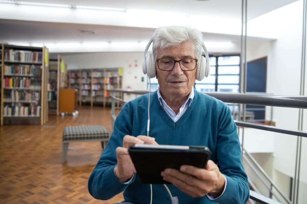 Ein Senior hört auf einem Tablet einen Podcast.