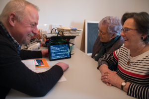 Ältere Menschen sitzen mit Tablets an einem Tisch.