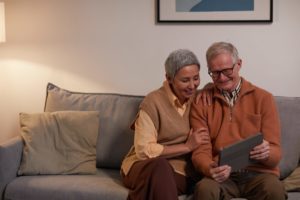 Zwei ältere Menschen sitzen nebeneinander auf dem Sofa und schauen auf ein Tablet