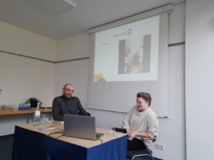 Der Referent und die Referentin sitzen vor der Powerpoint Präsentation