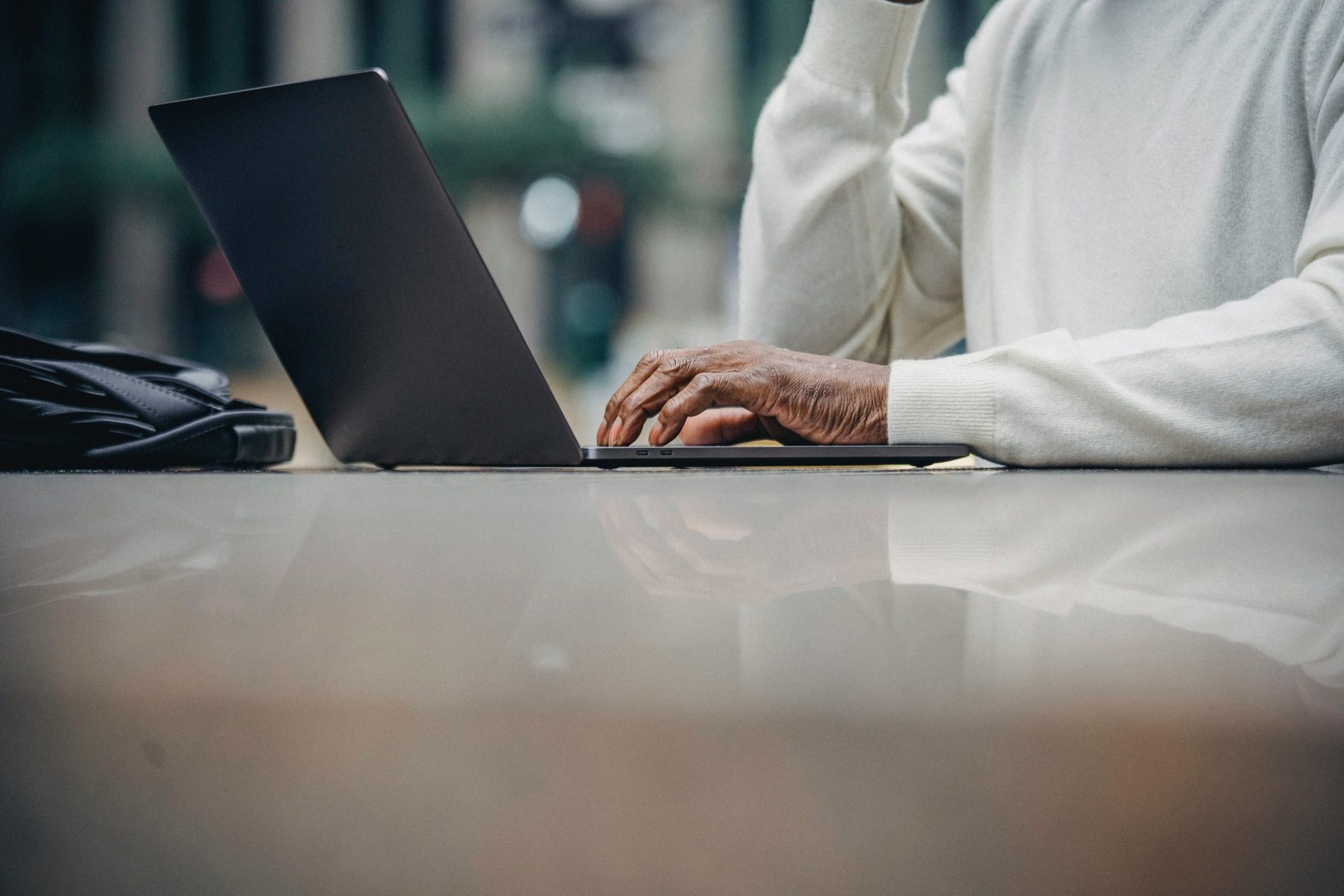 Das Bild zeigt einen aufkgelappten Laptop, dessen Bildschirm man nicht sieht und die Hand einer Person